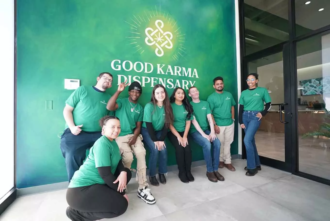 Eight people wearing green shirts pose in front of a green dispensary wall
