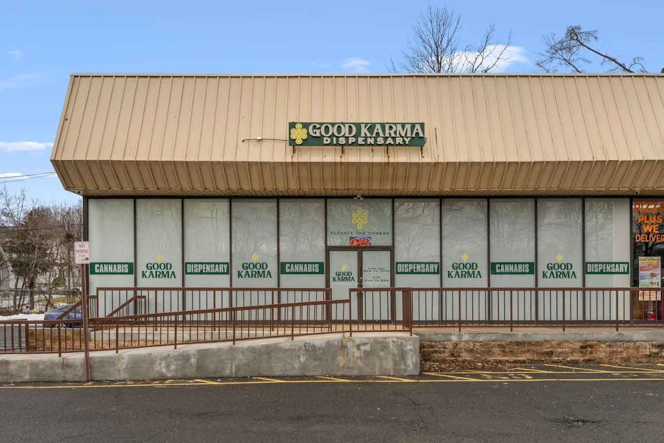 Tan building with green sign reading Good Karma Cannabis, covered windows, and metal railing
