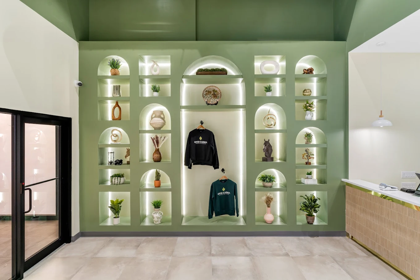 Green wall with recessed shelves containing various items including plants and clothing